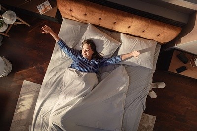 Above view of woman laying in bed with arms stretching out to each side